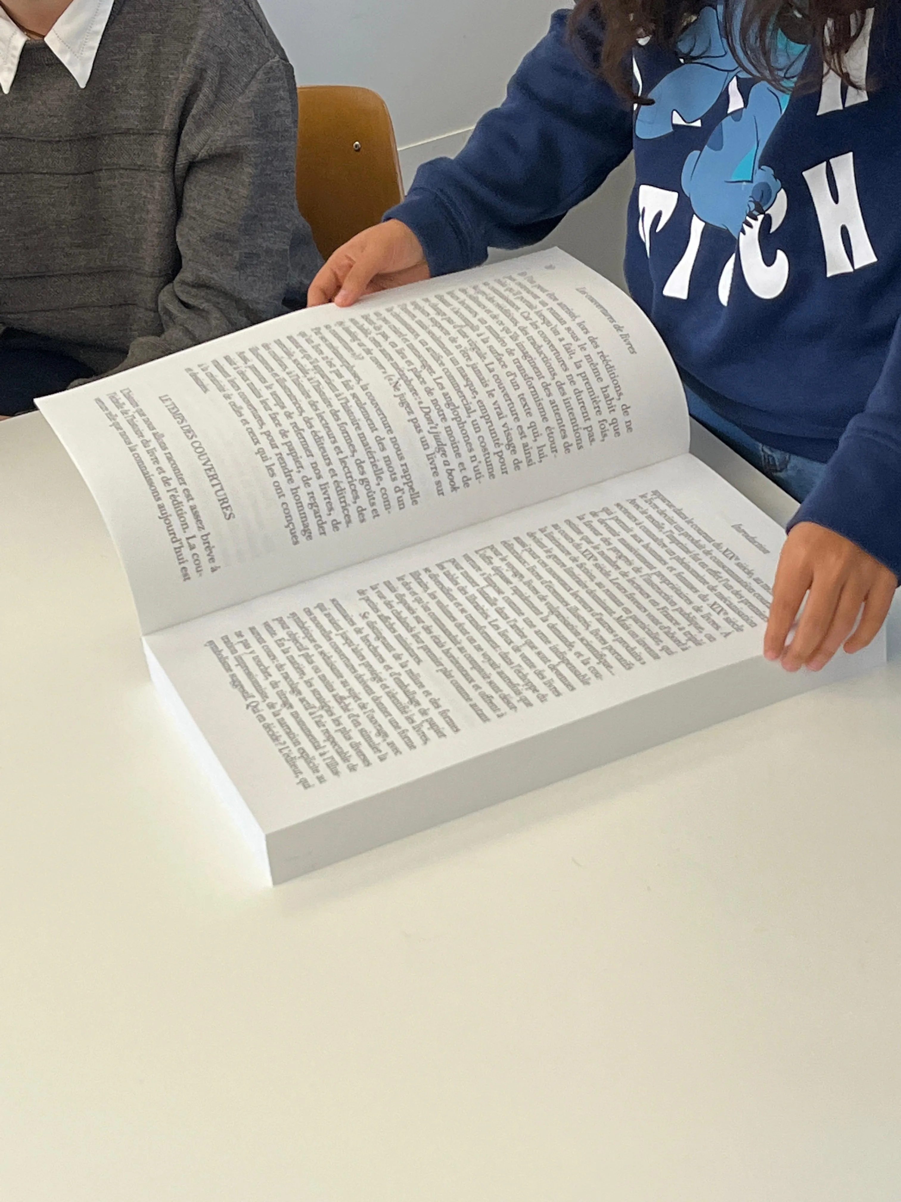 Lecture à deux du livre grand format ouvert sur une table.